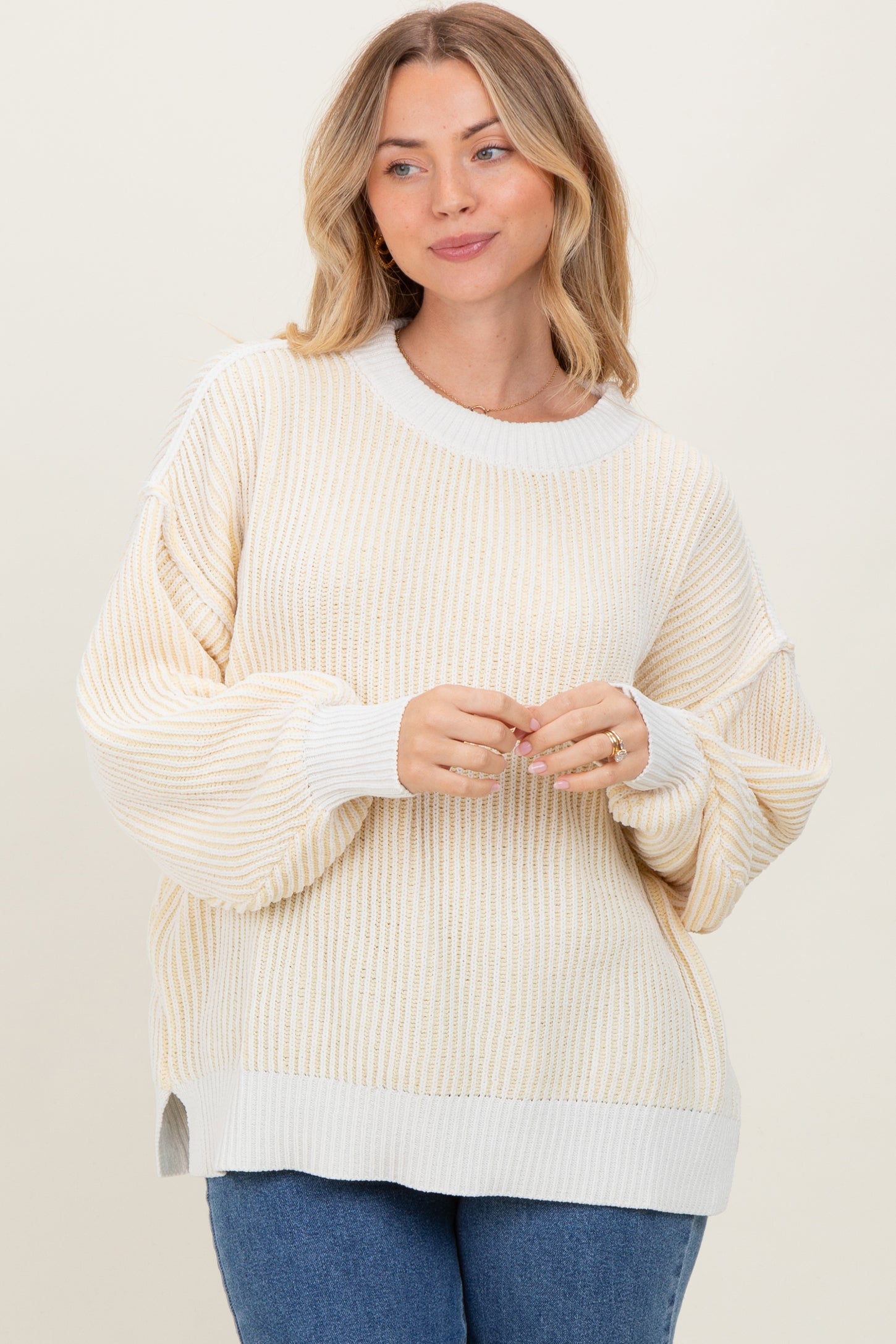 woman wearing a beige and white striped oversized sweater with balloon sleeves and side slits, smiling at the camera