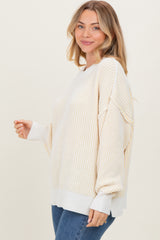 woman wearing a cream striped oversized sweater with ribbed details and a relaxed fit paired with blue jeans