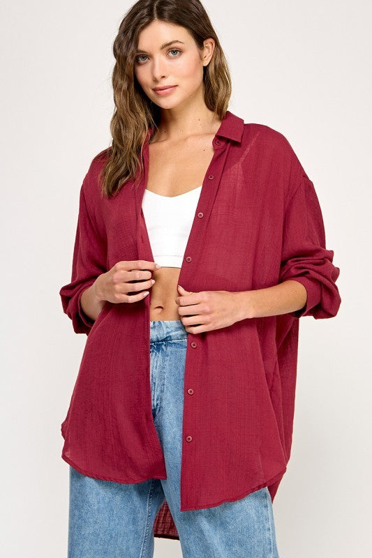 woman wearing a burgundy oversized button-up shirt and high-waisted jeans, posing with one hand on her waist