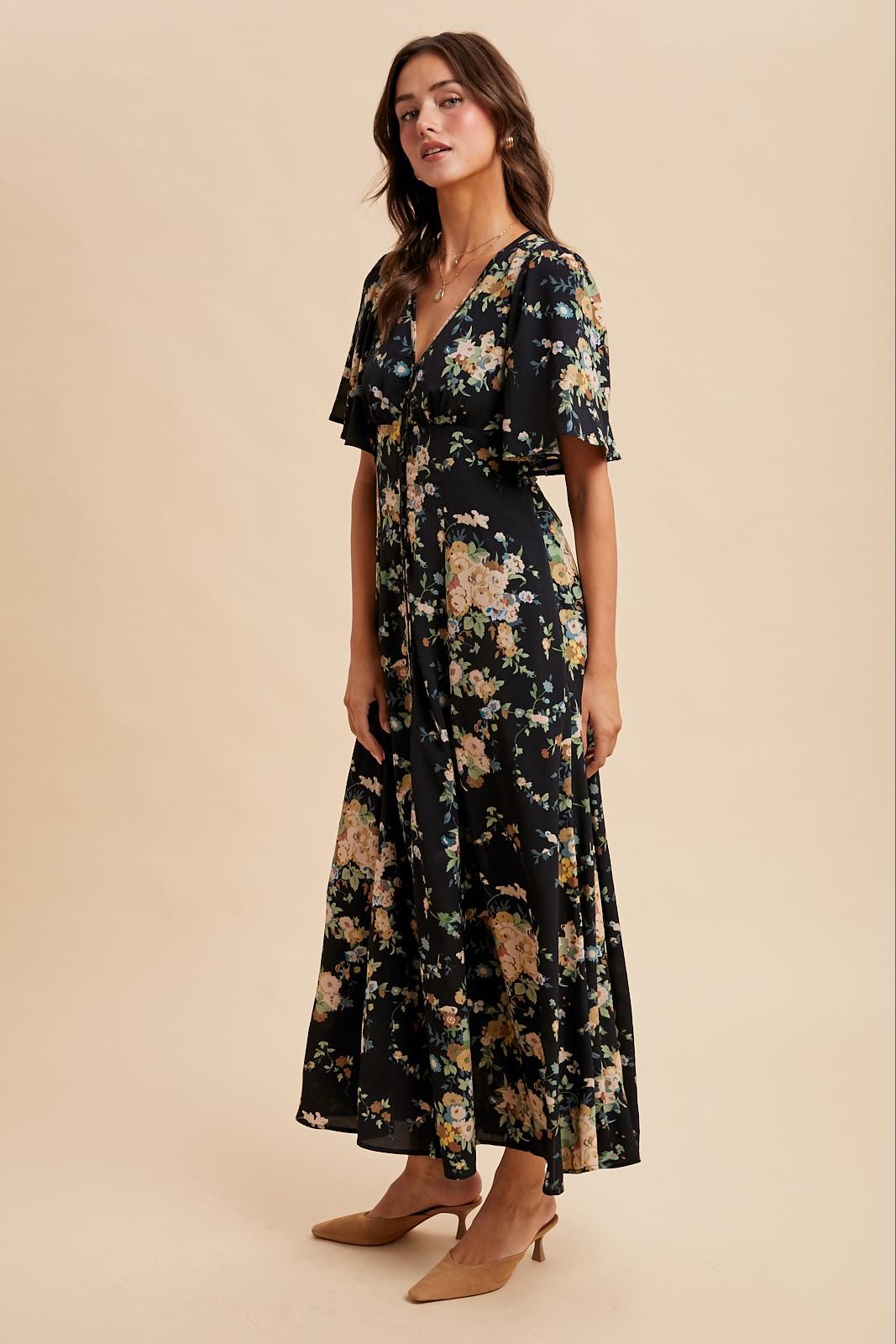 woman wearing a black floral maxi dress with flutter sleeves and a v-neckline, standing on a neutral background