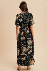 woman wearing a black floral maxi dress with short sleeves and a tied waist detail, seen from the back