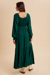 woman wearing a long green tiered maxi dress with long sleeves and a smocked waist, shown from the back