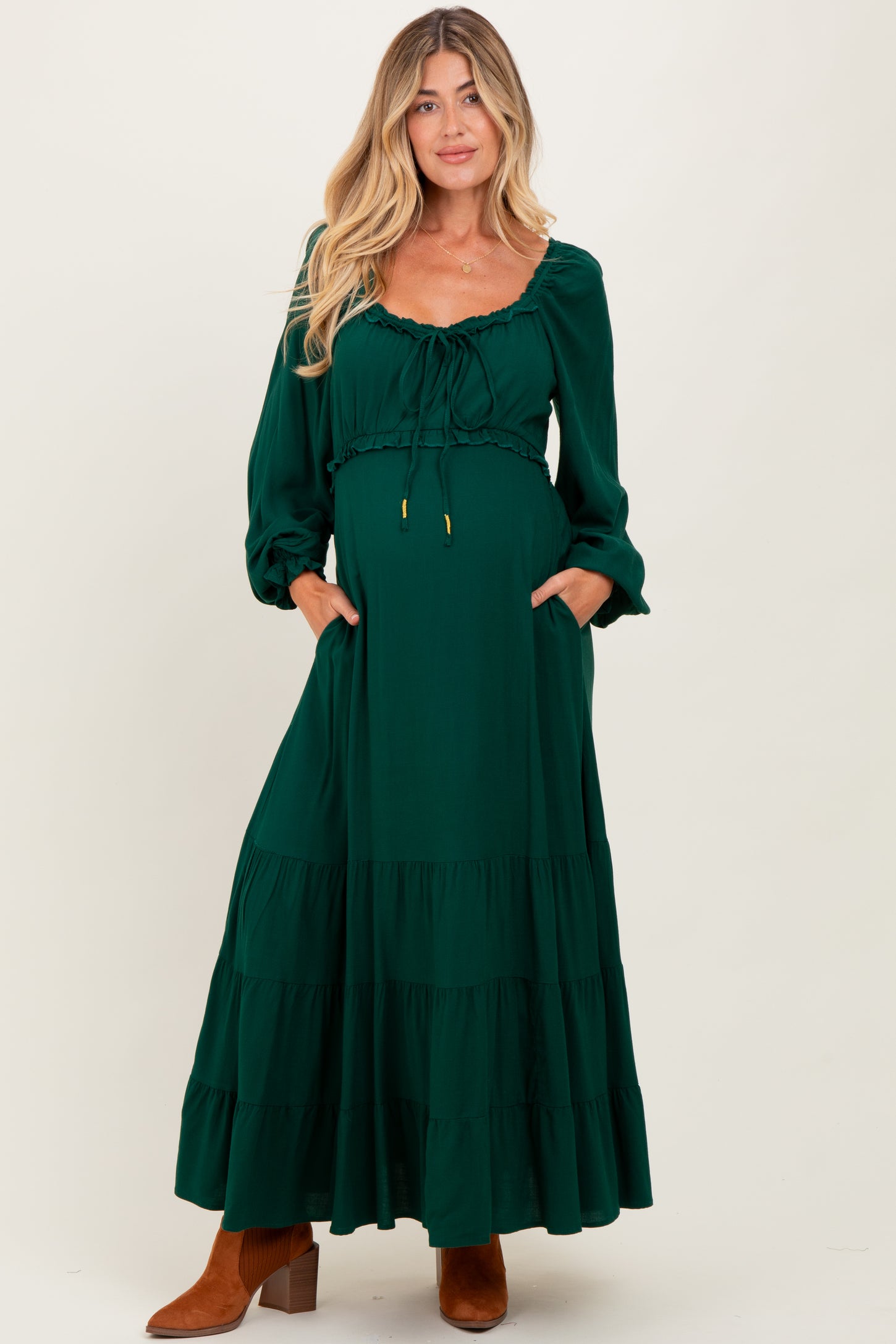 woman wearing a dark green maternity maxi dress with puffed sleeves and side pockets, highlighting her baby bump