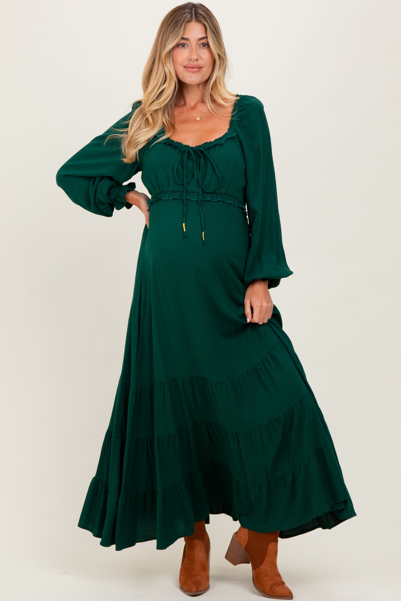 woman wearing a dark green maternity dress with long sleeves and ruffled hem, showcasing her baby bump