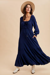 woman wearing a navy blue long sleeve maxi dress with a tie front detail and a wide-brimmed hat