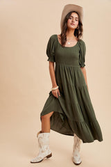 woman wearing an olive green puff sleeve maxi dress with a tiered skirt and standing in cowboy boots and a hat