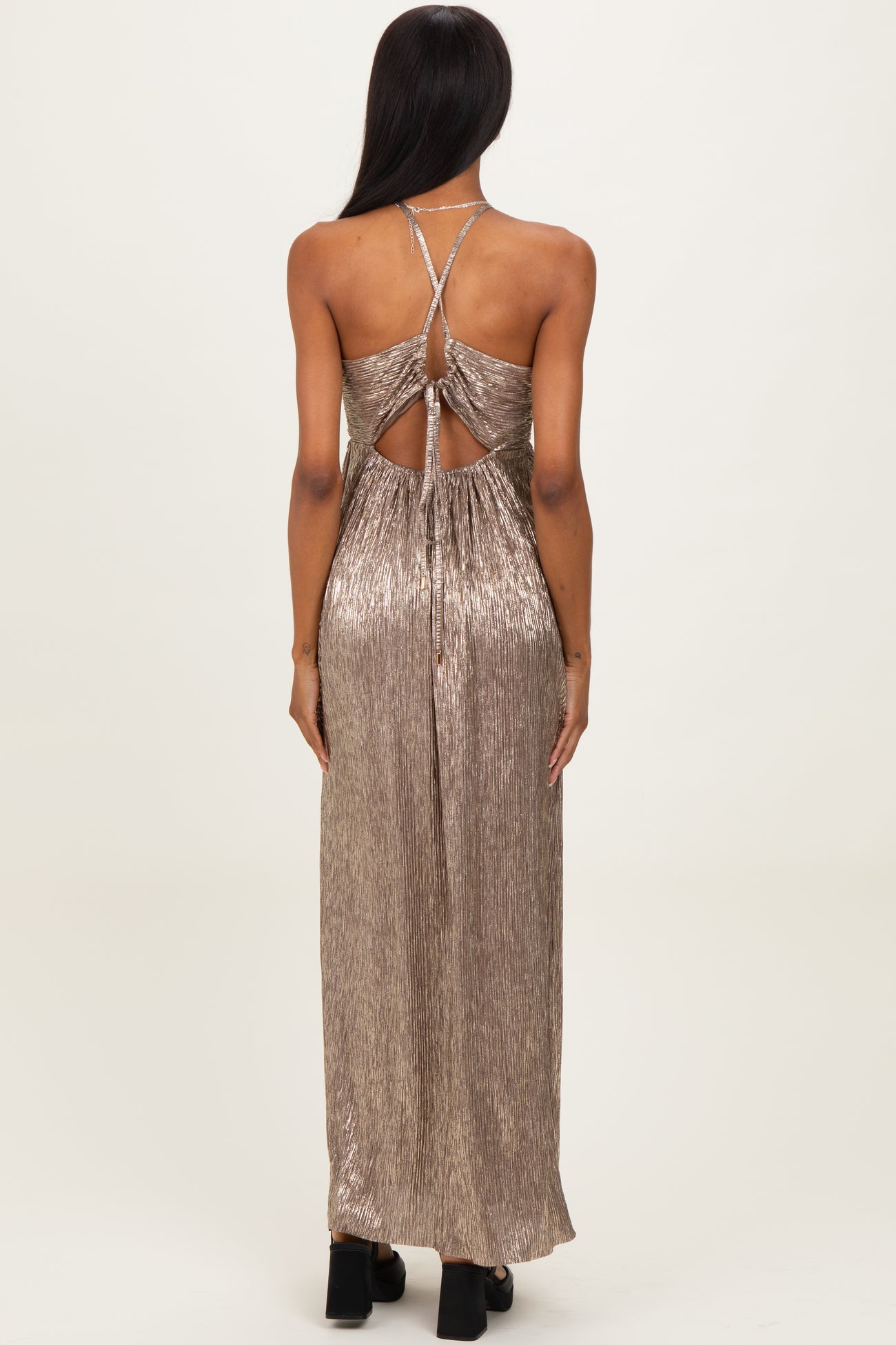 woman wearing a metallic gold backless maxi dress with crisscross straps and a flowing silhouette