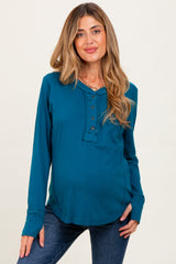 woman wearing a teal maternity long sleeve henley top with button detail and a visible baby bump