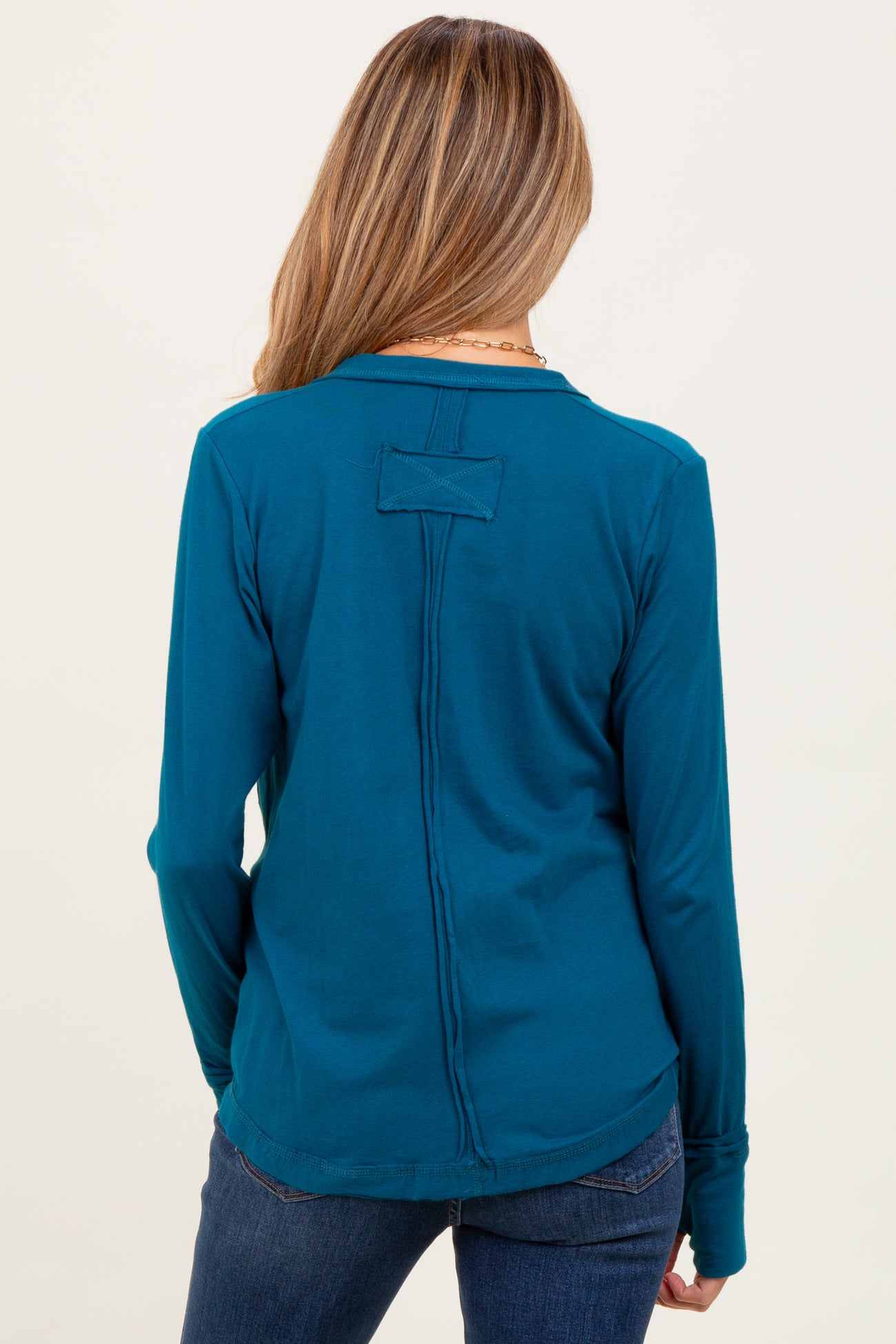 woman wearing a teal long sleeve maternity top with a stylish back detail and pairing it with jeans.