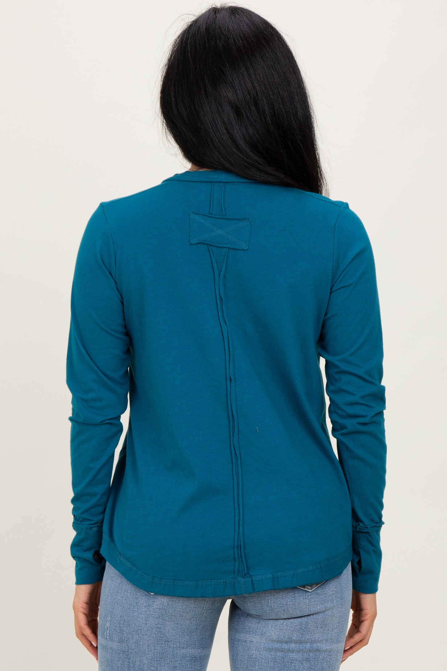 woman wearing a teal long sleeve top with a back seam detail, styled with light blue jeans