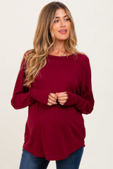 woman wearing a burgundy long sleeve maternity top with a curved hem and holding her baby bump