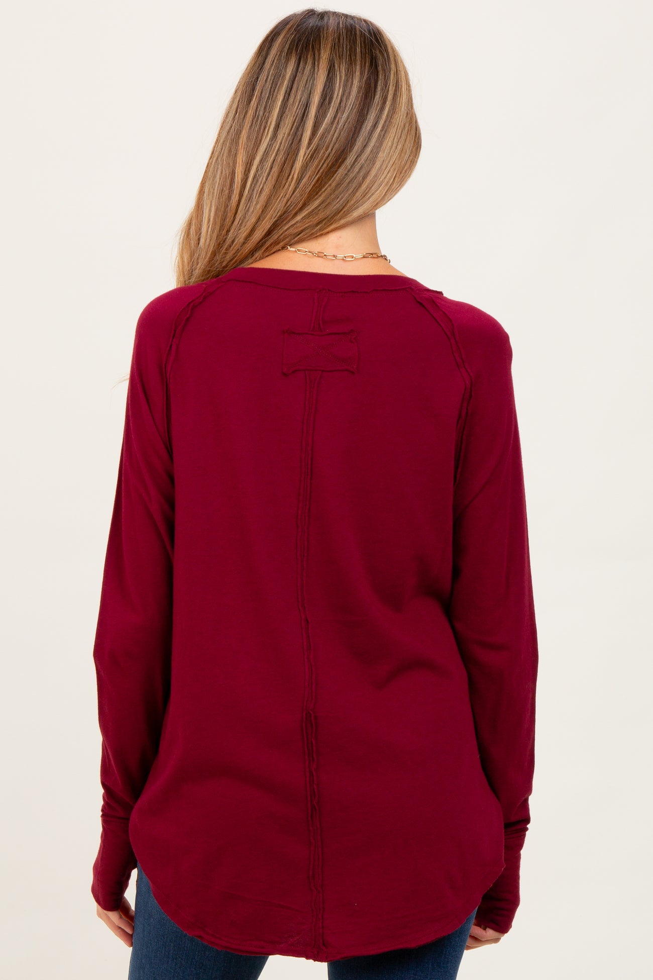 woman wearing a burgundy long sleeve maternity top with a back detail and relaxed fit
