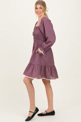 woman wearing a purple and pink checkered long sleeve dress with a gathered waist and ruffled hem