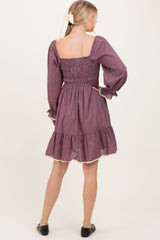 woman wearing a purple checkered smocked back dress with long sleeves and a ruffled hem