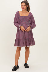 woman wearing a purple checkered maternity dress with a smocked bodice and tiered skirt, holding her baby bump