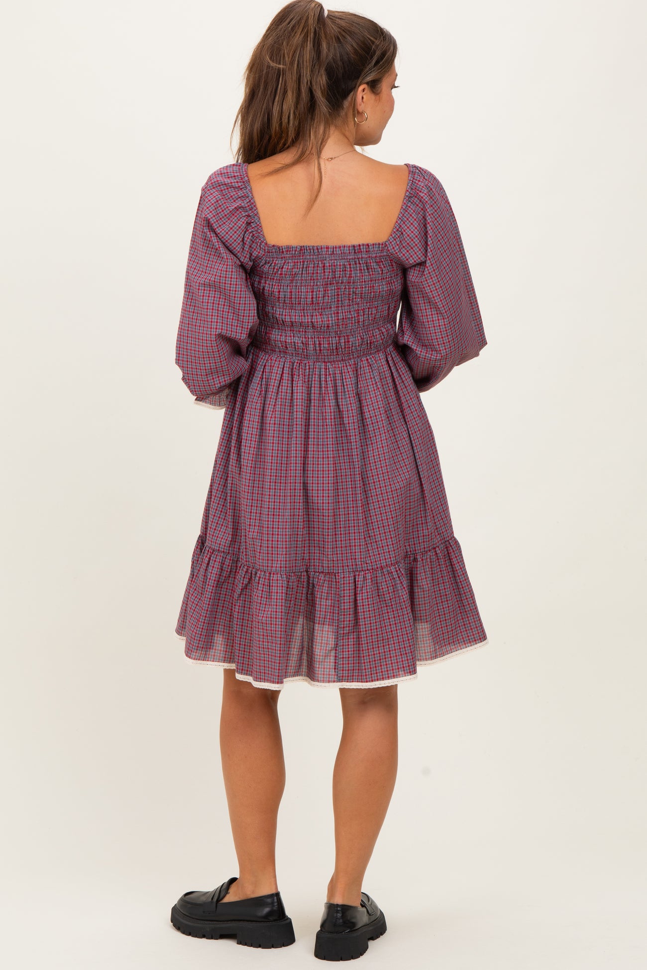 woman wearing a purple checkered maternity dress with puffed sleeves and a tiered skirt, showing a baby bump