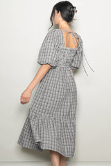 woman wearing a black and white gingham midi dress with puff sleeves and a tied open back detail