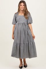 woman wearing a black and white checkered maternity dress with puff sleeves and tiered skirt, showcasing her baby bump