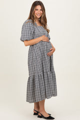 woman wearing a black and white checkered maternity dress with puff sleeves and a tiered skirt, holding her baby bump