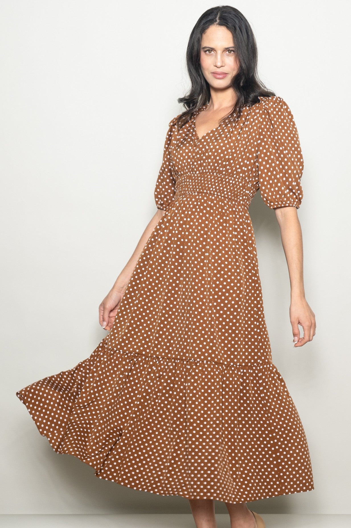 woman wearing a brown polka dot maxi dress with a fitted bodice and puff sleeves, smiling while posing
