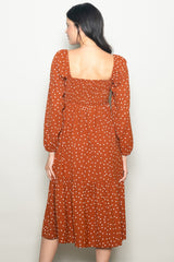 woman wearing a rust colored polka dot dress with a smocked bodice and tiered skirt, shown from the back