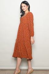 woman wearing a rust-colored midi dress with white polka dots and long sleeves, styled with a tiered skirt