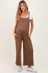 woman wearing a brown maternity jumpsuit with pockets and a white t-shirt underneath, displaying a baby bump