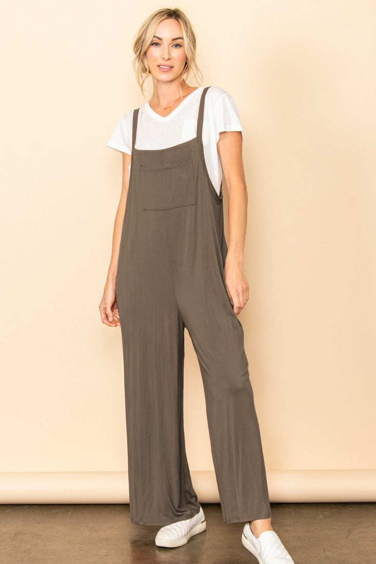 woman wearing a brown sleeveless jumpsuit over a white t-shirt with a front pocket and white sneakers