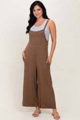woman wearing a brown sleeveless jumpsuit with wide legs and front pockets, paired with a gray tank top