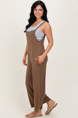woman wearing a brown sleeveless jumpsuit over a gray tank top, standing sideways with long wavy hair