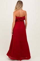 woman wearing a burgundy strapless maternity maxi dress with ruffle detail and pleated skirt from the back