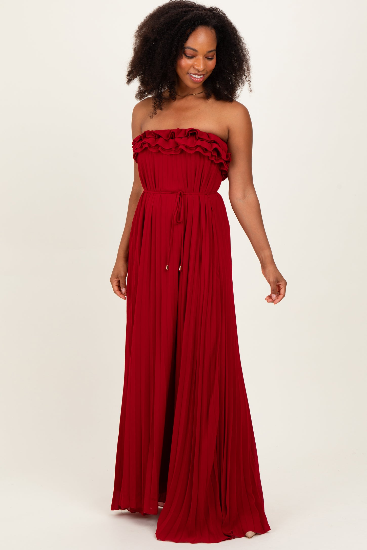 woman wearing a flowy red strapless maxi dress with ruffle details and a cinched waist.