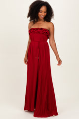 woman wearing a flowy red strapless maxi dress with ruffle details and a cinched waist.