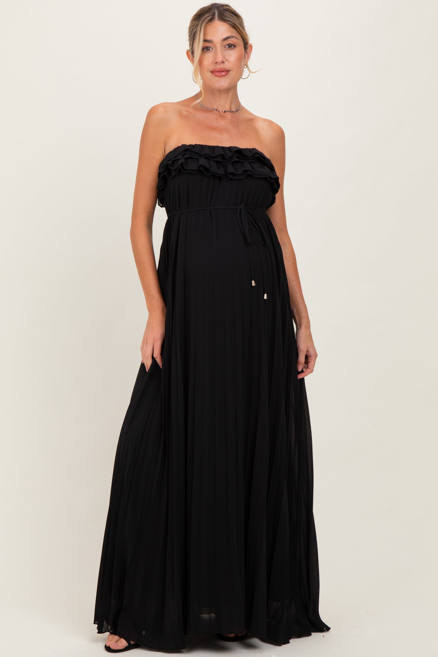 woman wearing a black strapless maternity maxi dress with ruffle detail and a flowing pleated skirt, showing baby bump