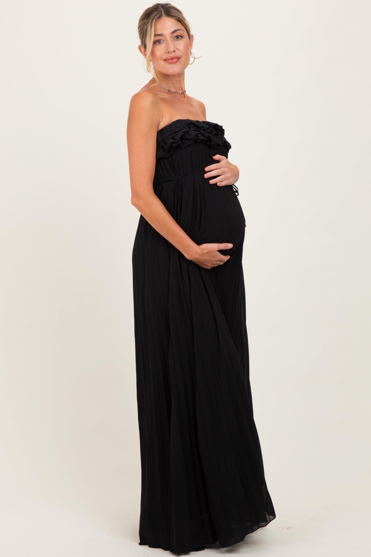 woman wearing a black strapless maternity maxi dress with ruffle detailing and holding her baby bump