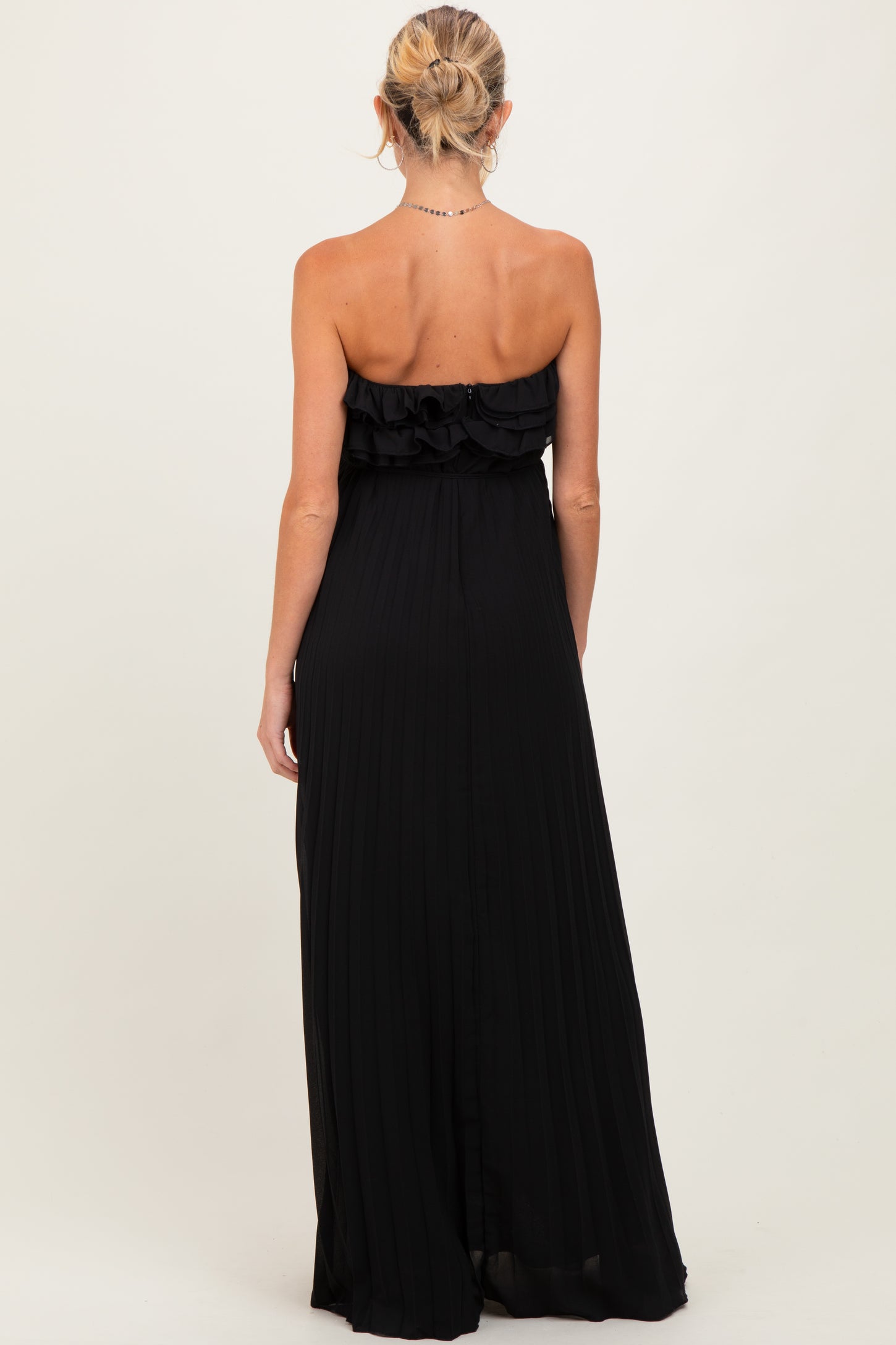 woman wearing a black strapless maternity maxi dress with ruffle detailing and pleated fabric