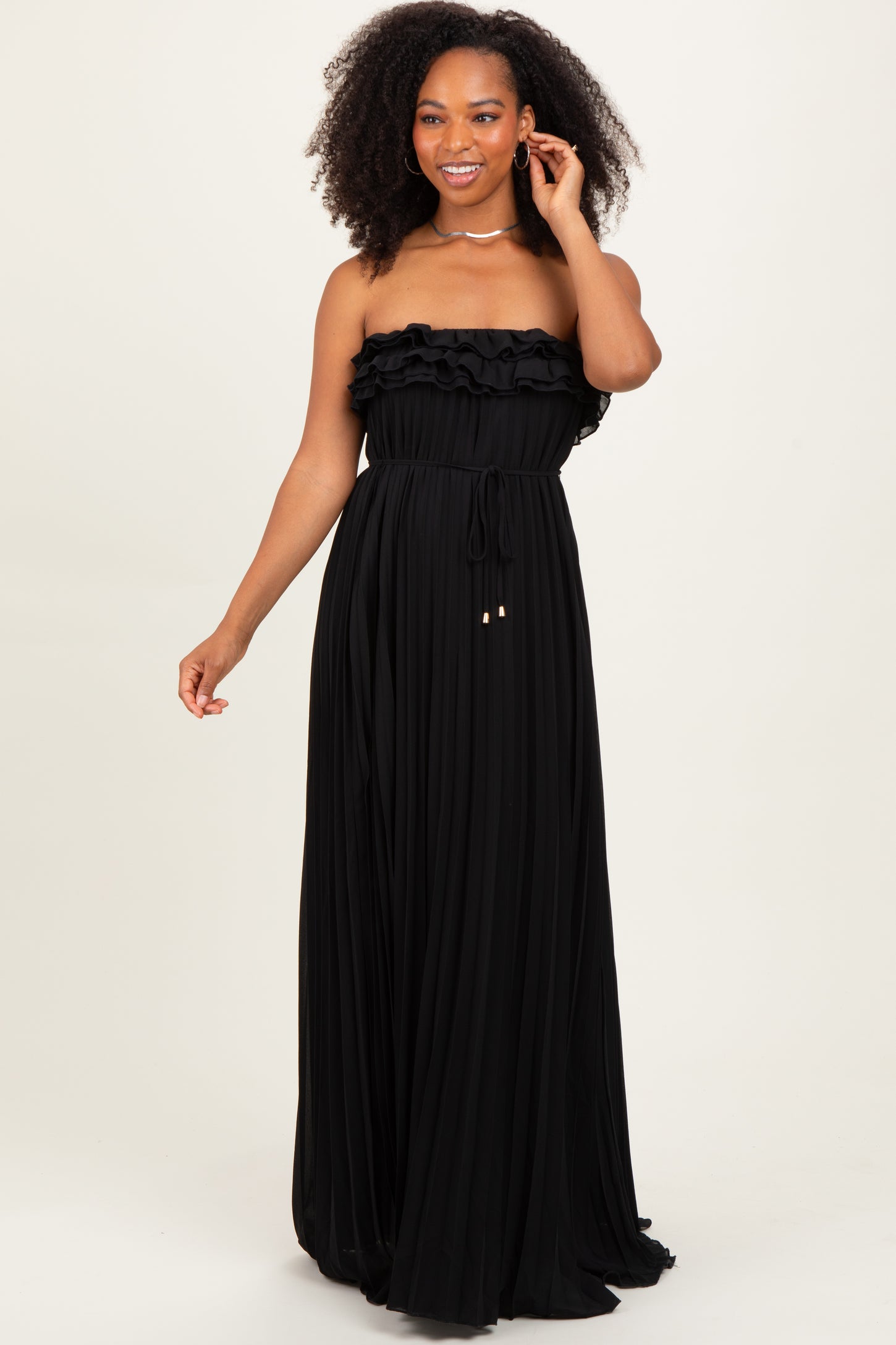woman wearing a black strapless maxi dress with ruffle details and a cinched waist, posing gracefully