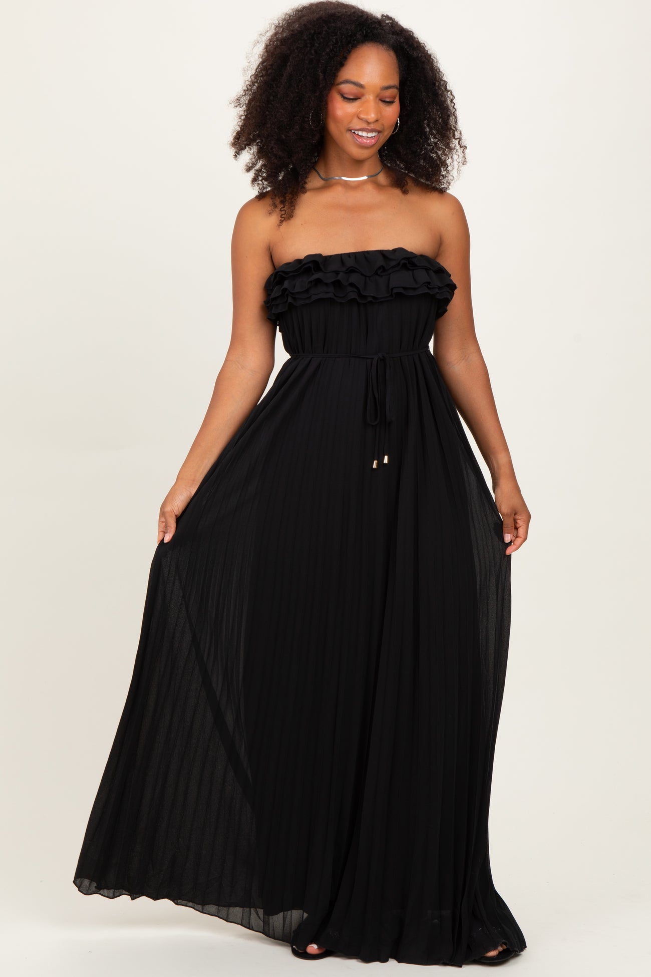 woman wearing a black strapless maxi dress with ruffle details and a tie waist