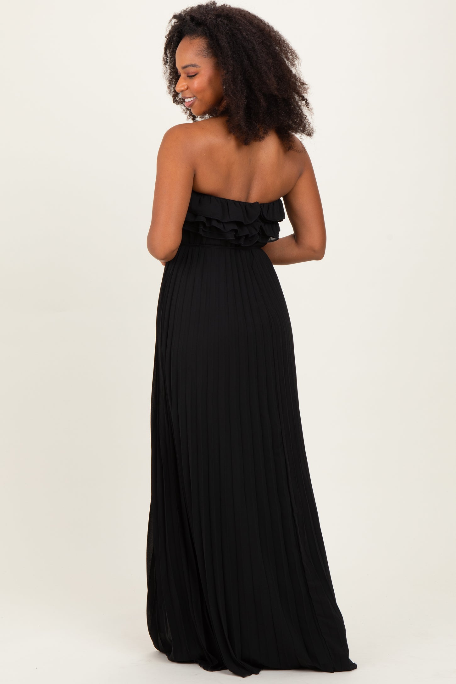 woman wearing a black strapless maxi dress with ruffle detailing and pleated fabric, viewed from the back