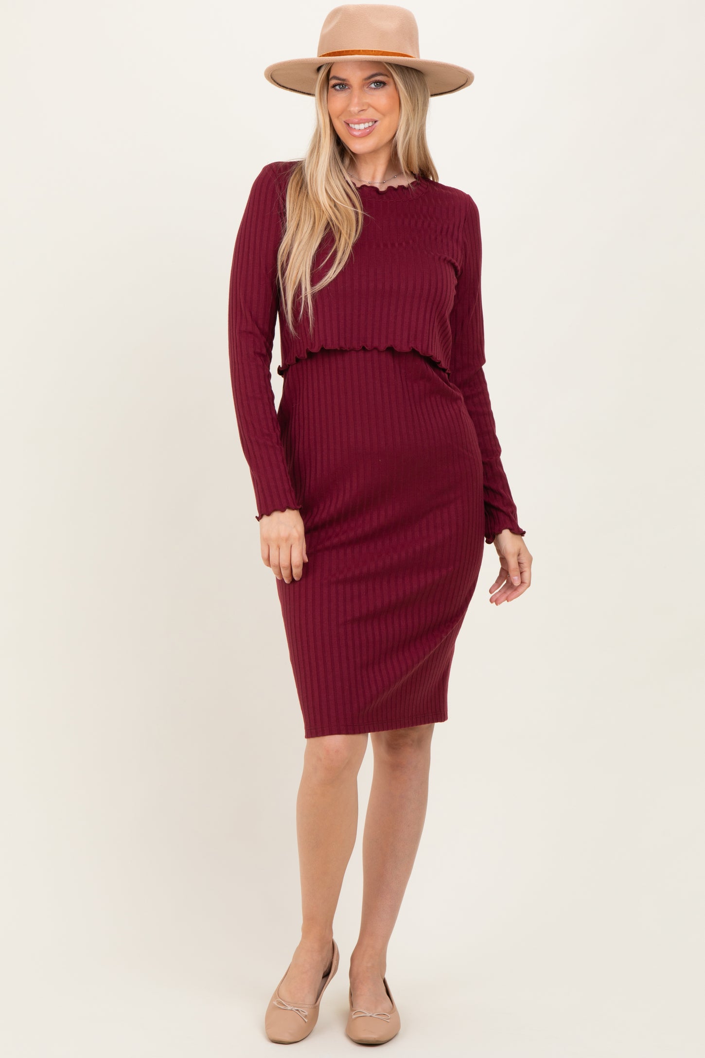 woman wearing a burgundy ribbed long sleeve dress with a ruffled waist and a wide-brimmed hat