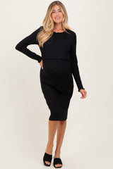 woman wearing a black ribbed maternity dress with a fitted silhouette and long sleeves, showing her baby bump