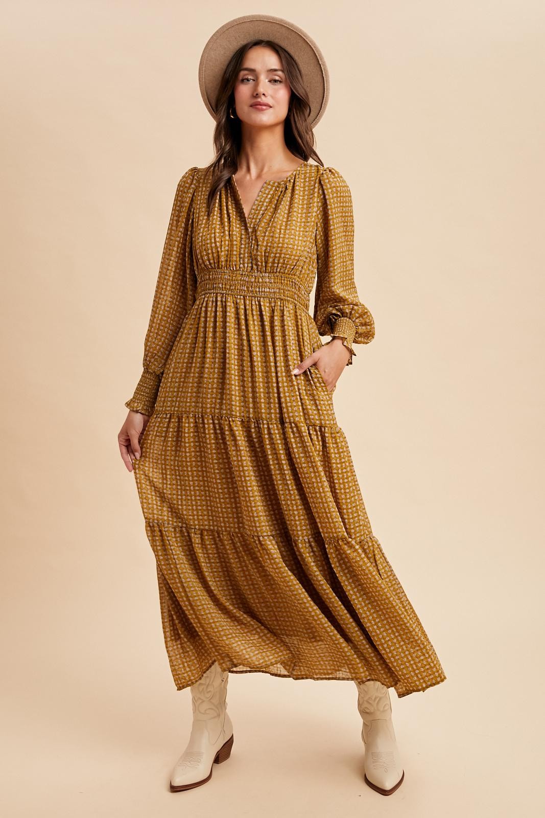 woman wearing a mustard yellow tiered maxi dress with long sleeves and a smocked waist, accessorized with a wide-brim hat