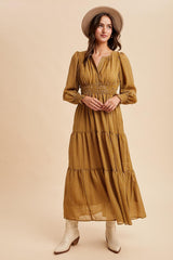 woman wearing a mustard yellow long sleeve maxi dress with a smocked waist and tiered skirt, accessorized with a tan hat and white boots