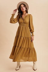 woman wearing a mustard yellow long sleeve maxi dress with tiered detailing and a smocked waist, paired with a wide-brimmed hat and ankle boots