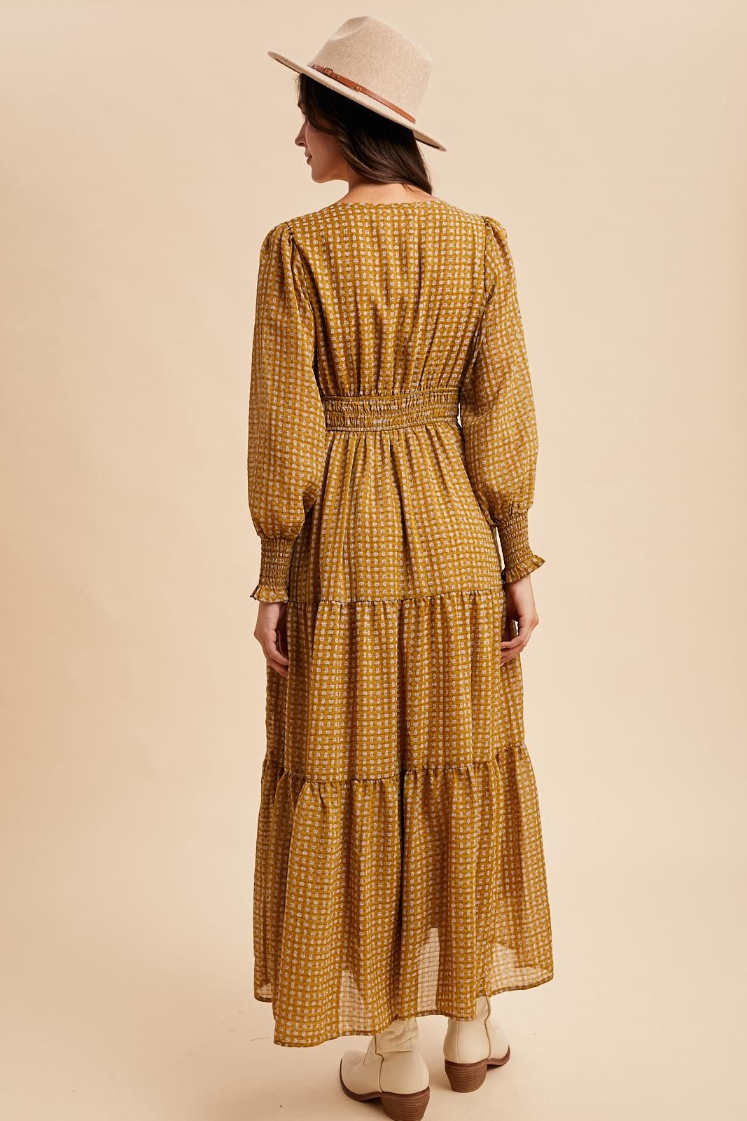 woman wearing a mustard yellow long sleeve tiered maxi dress with a cinched waist and patterned design, standing with her back facing the camera