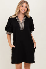 woman wearing a black puff sleeve dress with a plaid neckline and side pockets