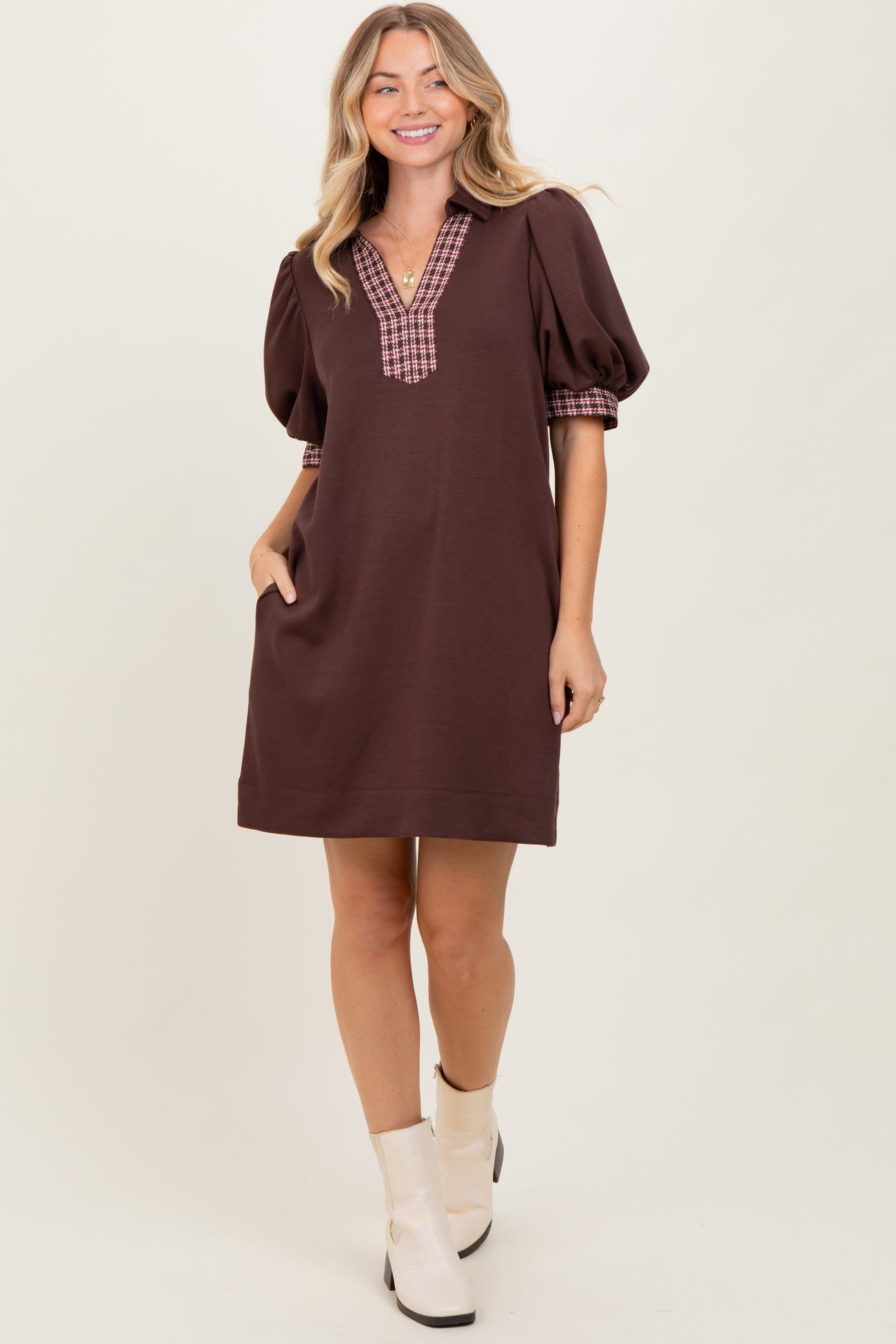 woman wearing a brown puff sleeve dress with a plaid neckline and pockets, standing against a neutral background