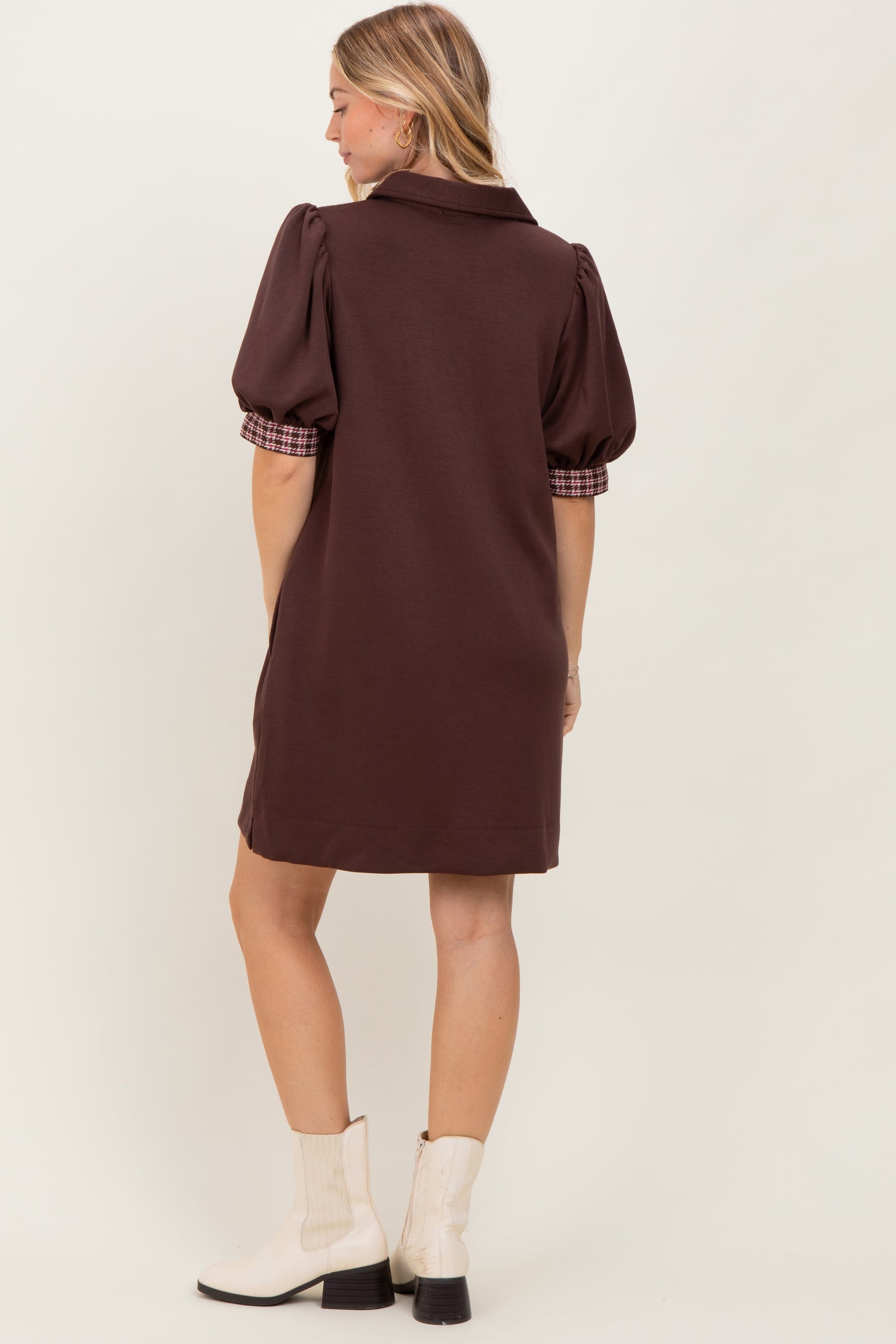 woman wearing a brown short dress with puff sleeves and checkered detail at the cuffs, viewed from the back