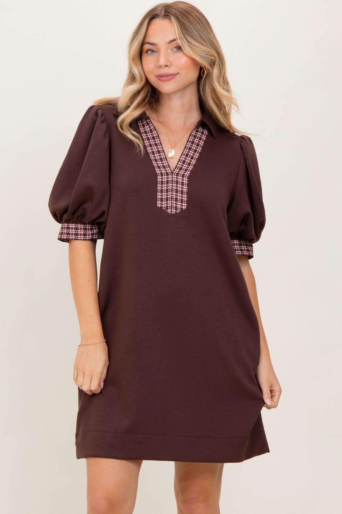 woman wearing a brown short sleeve dress with puff sleeves and plaid detail on the cuffs