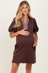 woman wearing a brown maternity dress with puffy sleeves and a plaid neckline, gently holding her baby bump